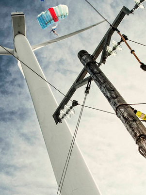 Person in yellow safety jacket working on a power line with a blue sky and white clouds in the background.