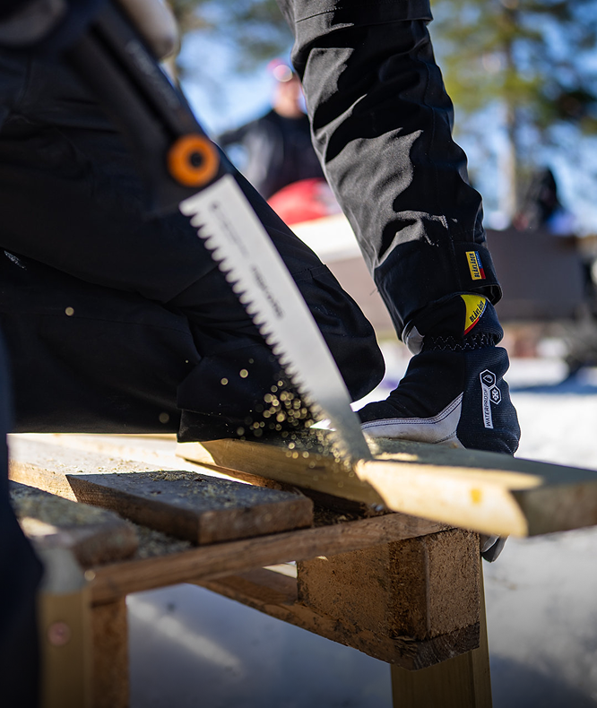 Person using a handsaw to cut wood on a wooden platform with a blurred background