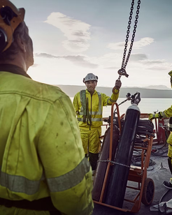 Workers in high-visibility clothing on a ship with equipment and ocean in the background