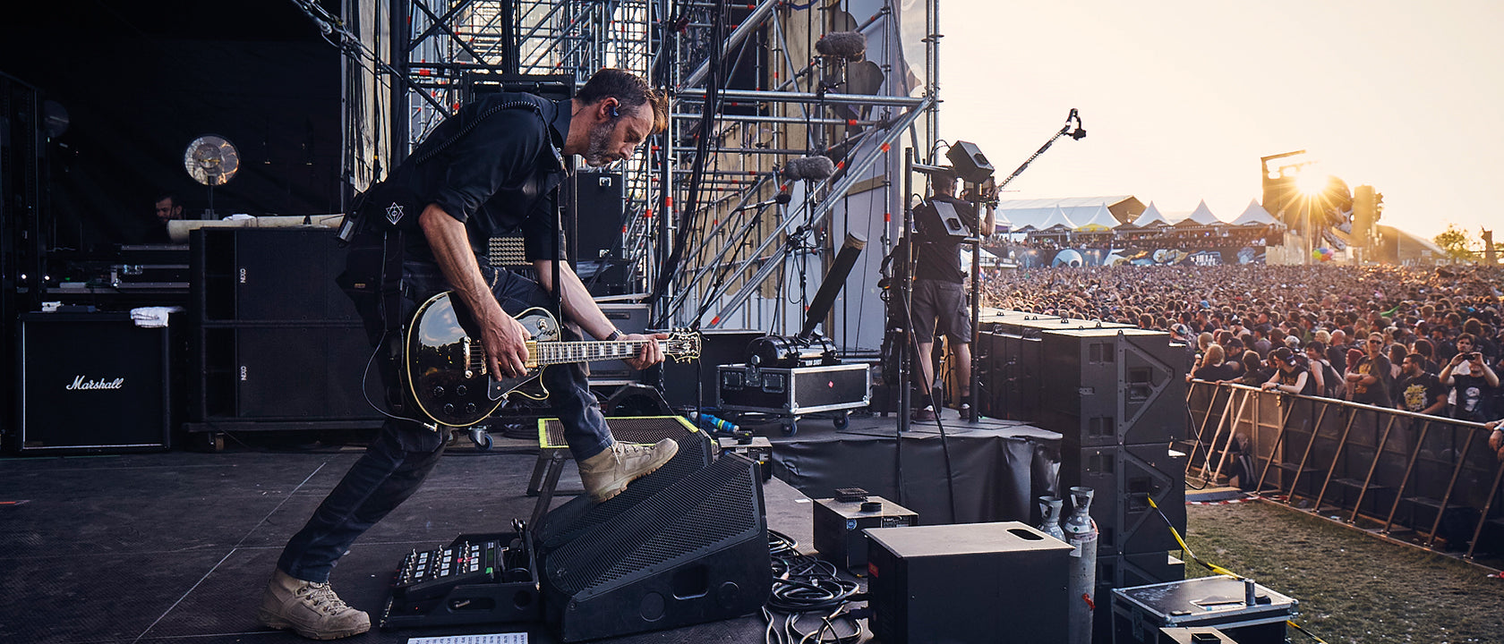 Musician playing guitar on stage at a concert with a crowd and equipment in the background