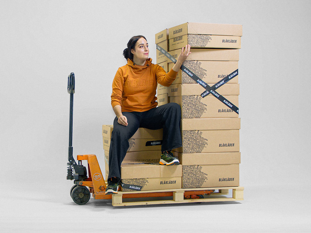 Person sitting on a stack of boxes with a forklift, on a plain background